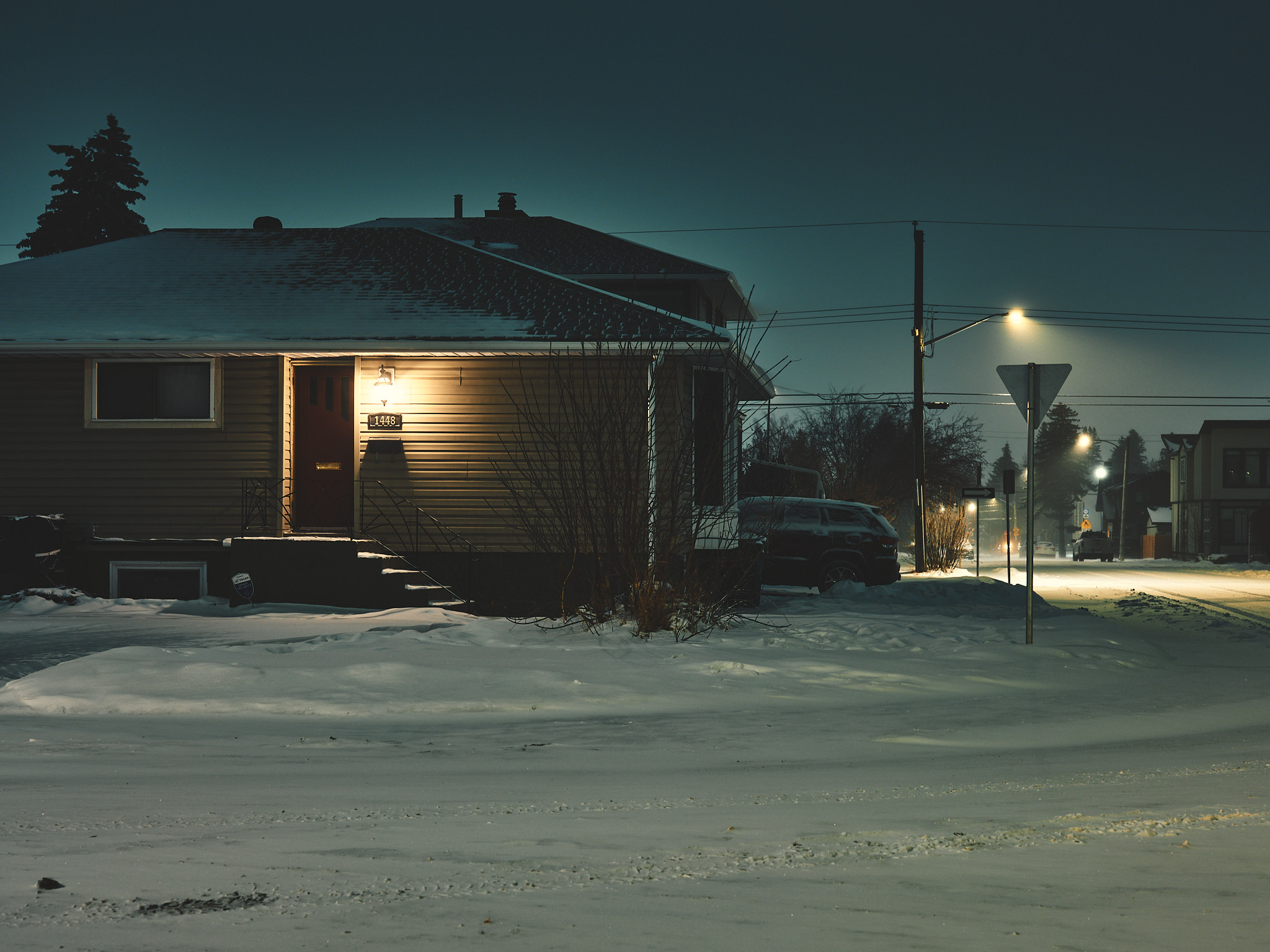 Small prairie house at night with porch light glowing in deep snow