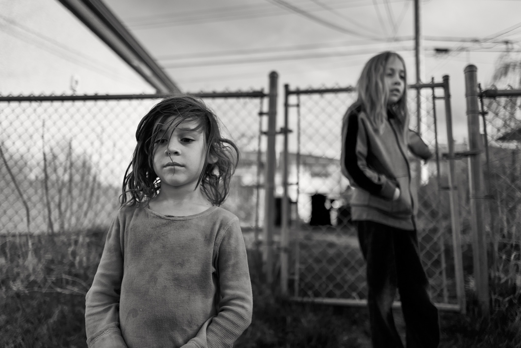 Two children near a chain-link fence in a yard, black and white documentary