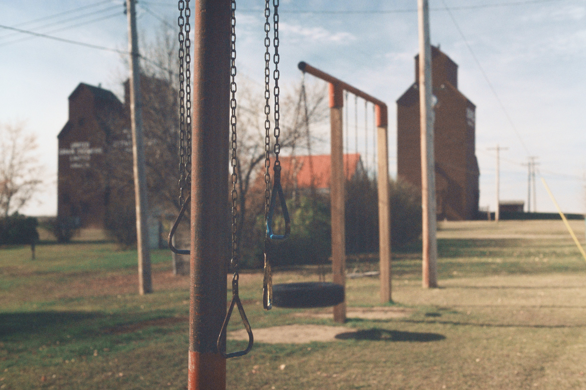 Playground swings and tire swing with grain elevators in the background, medium format film