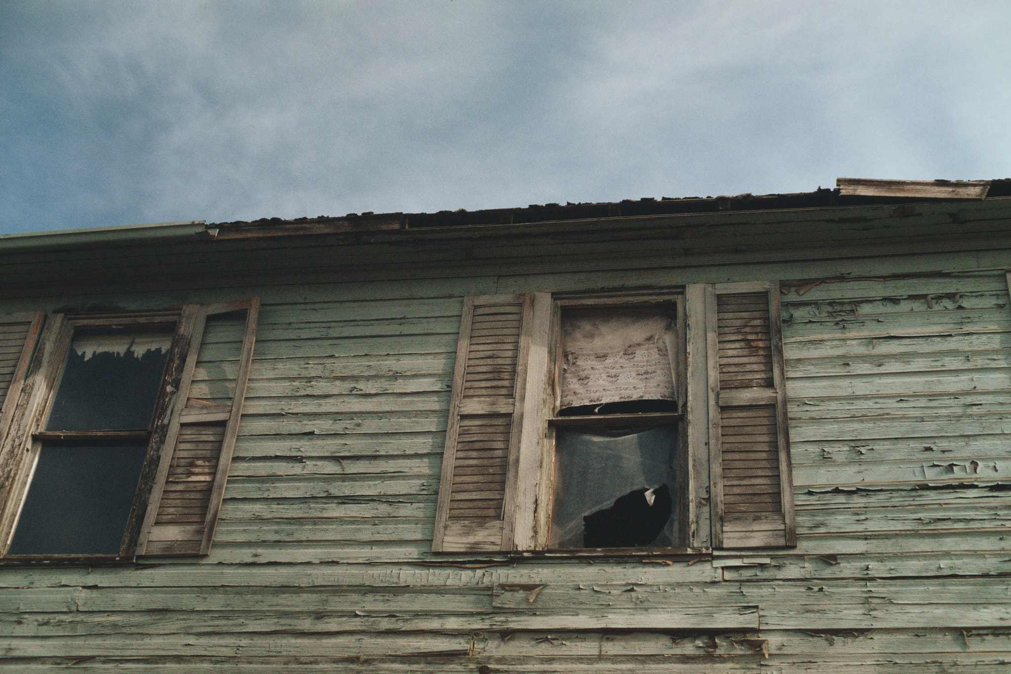 Weathered clapboard building with broken windows and peeling paint