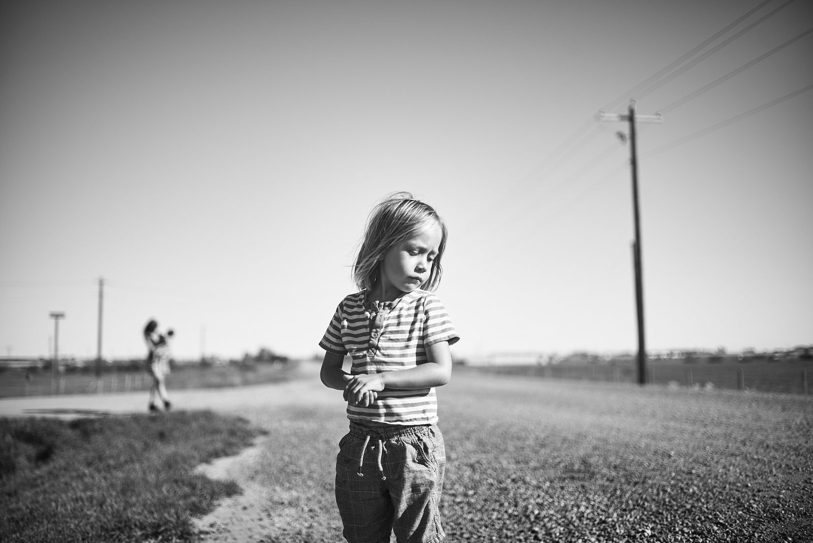 Child walking along a prairie road with power lines stretching to the horizon, black and white