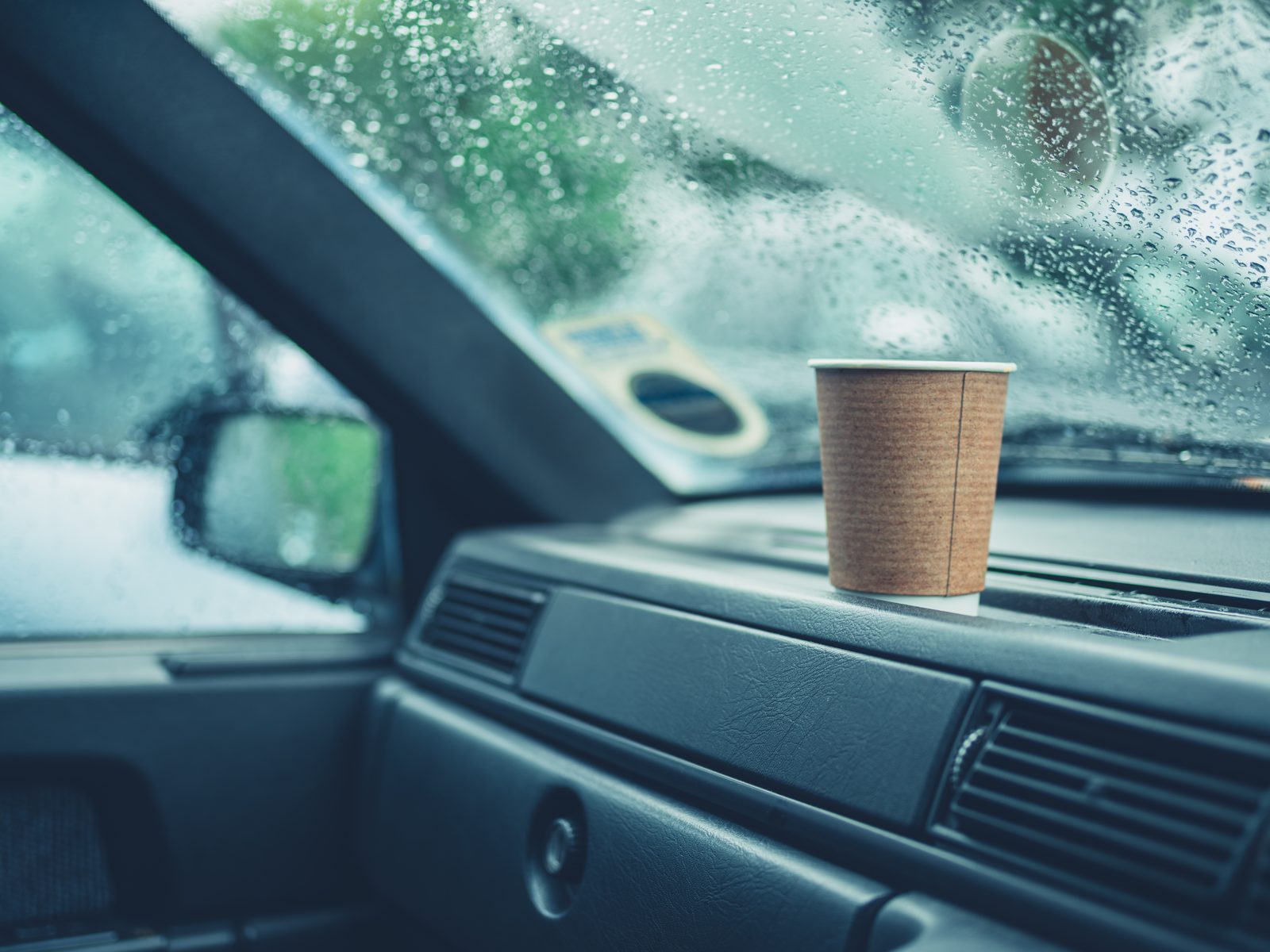 Coffee cup on car dashboard on a rainy day — moody lifestyle photography