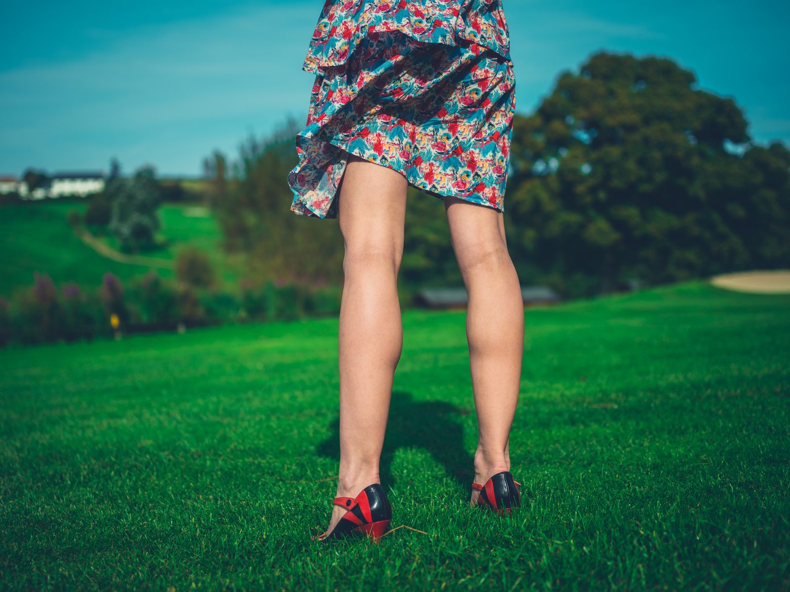 Legs and heels on green lawn with dress blowing in wind — fashion editorial photography
