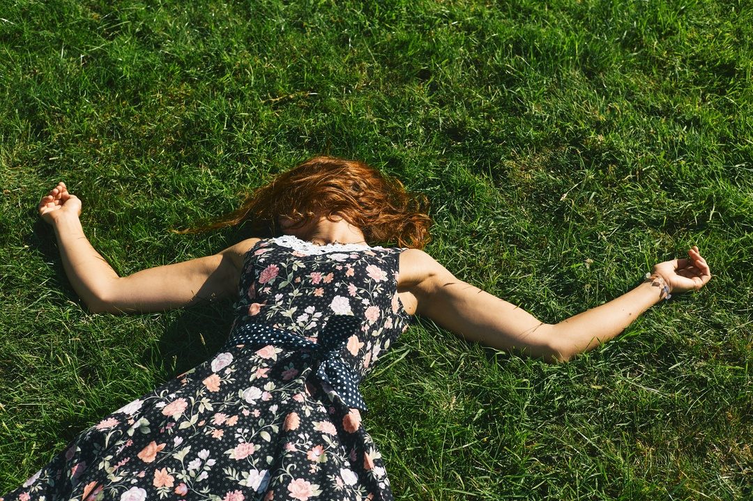 Red-haired woman in floral dress lying on grass — natural light portrait photography