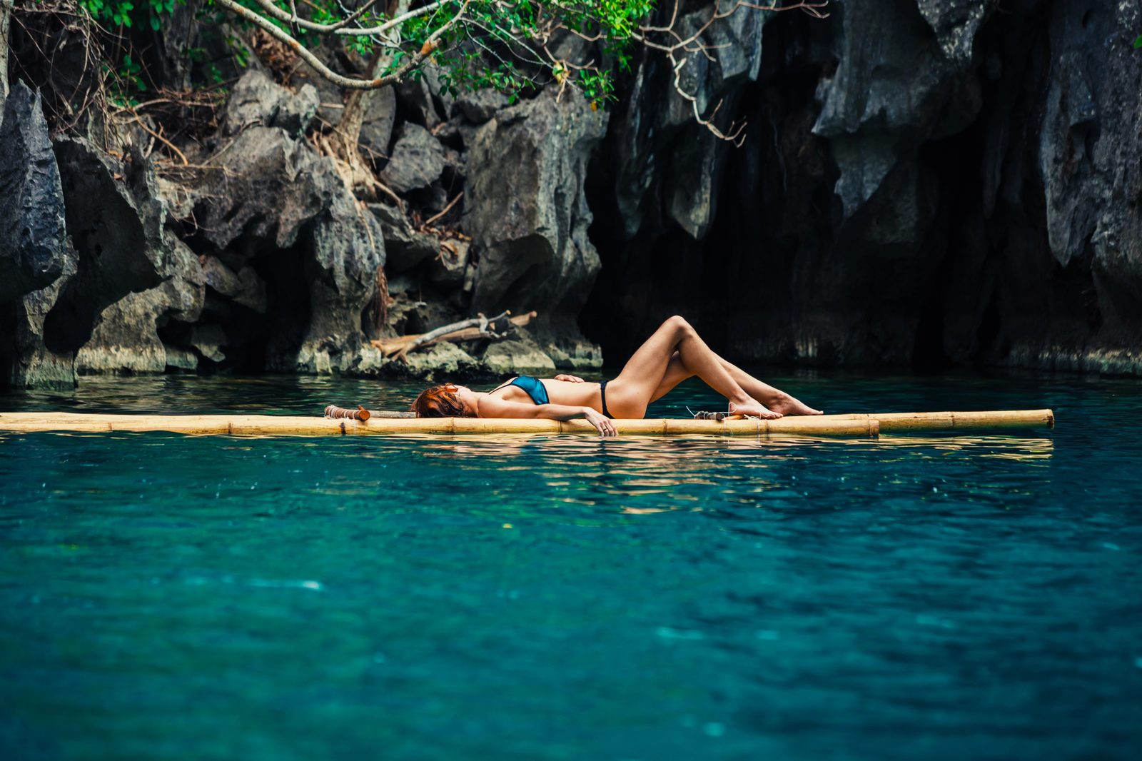 Woman sunbathing on bamboo raft in turquoise lagoon — tropical travel photography