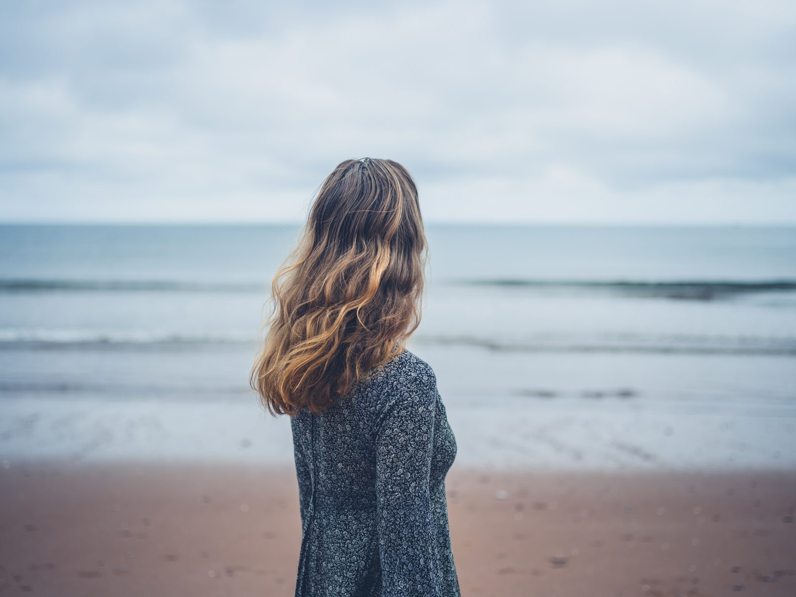 Woman in dress admiring the ocean — moody coastal portrait photography